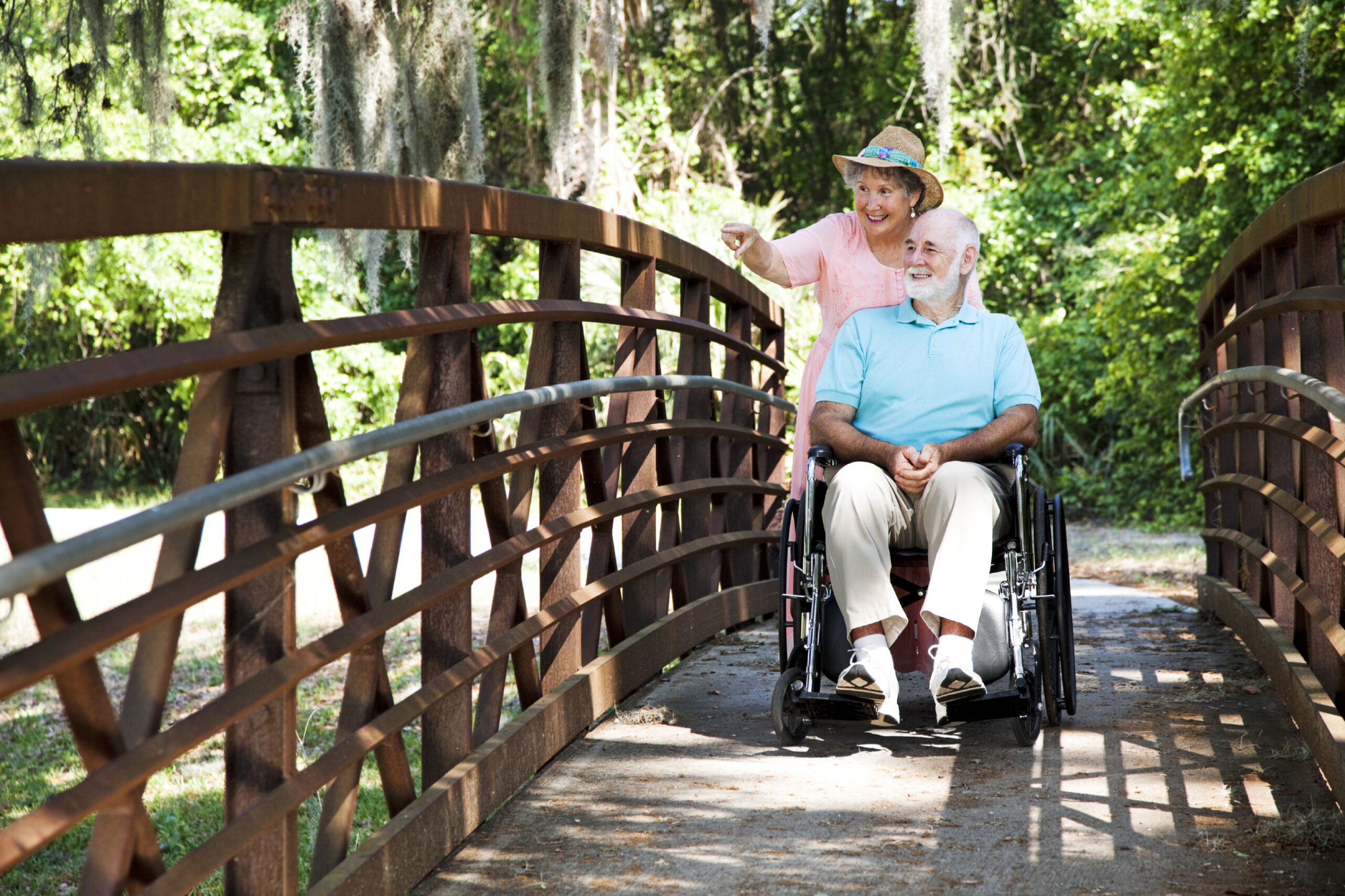 Senior woman pushing her disabled husband through the park in his wheelchair.